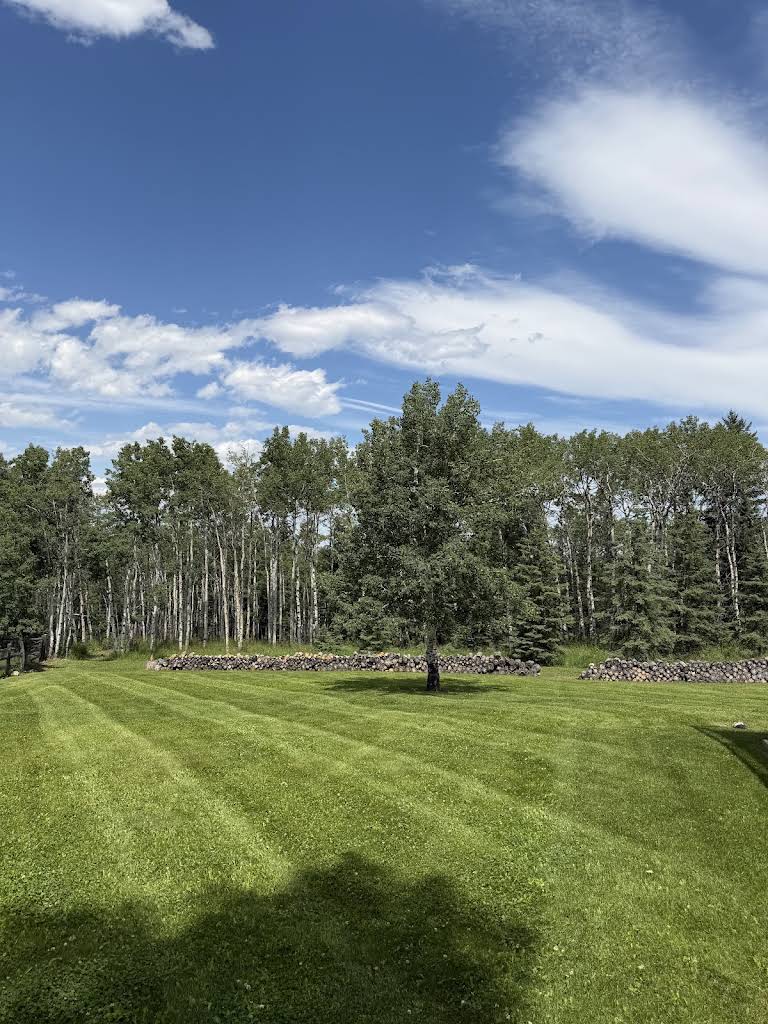 Fresh mowing stripes on an acreage lawn bordered by trees and a stone wall